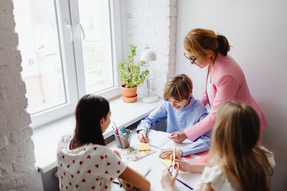 A teacher assists students with schoolwork around a desk in a bright classroom.